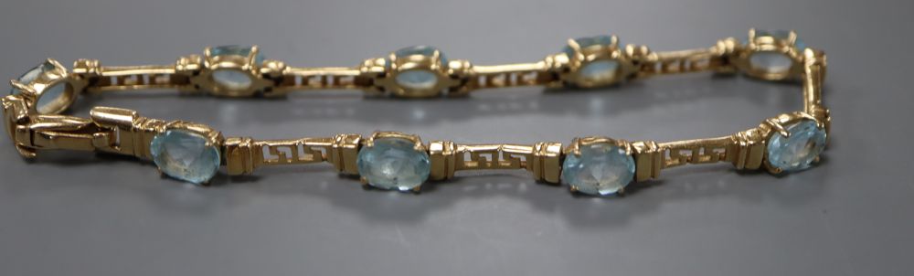 A modern 585 yellow metal and nine stone oval cut blue topaz set bracelet, 21.5cm, gross 16.8 grams.